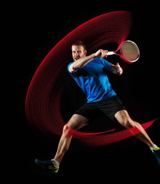 The one caucasian man playing tennis isolated on black background. Studio shot of fit young player at studio in motion or movement during sport game with led light trail