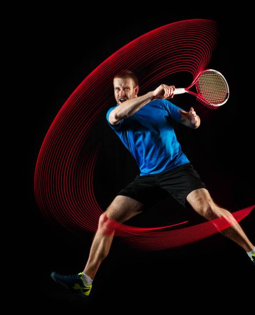 The one caucasian man playing tennis isolated on black background. Studio shot of fit young player at studio in motion or movement during sport game with led light trail