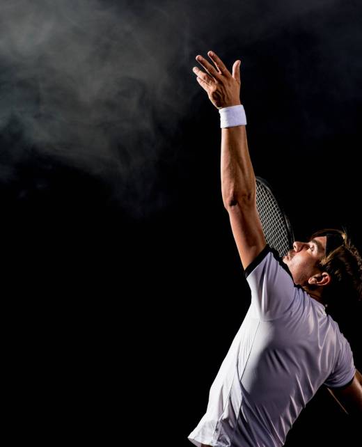 Male caucasian tennis player serving on a black background.