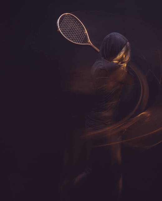 motion shot of woman exercising with tennis racket in hands isolated on black